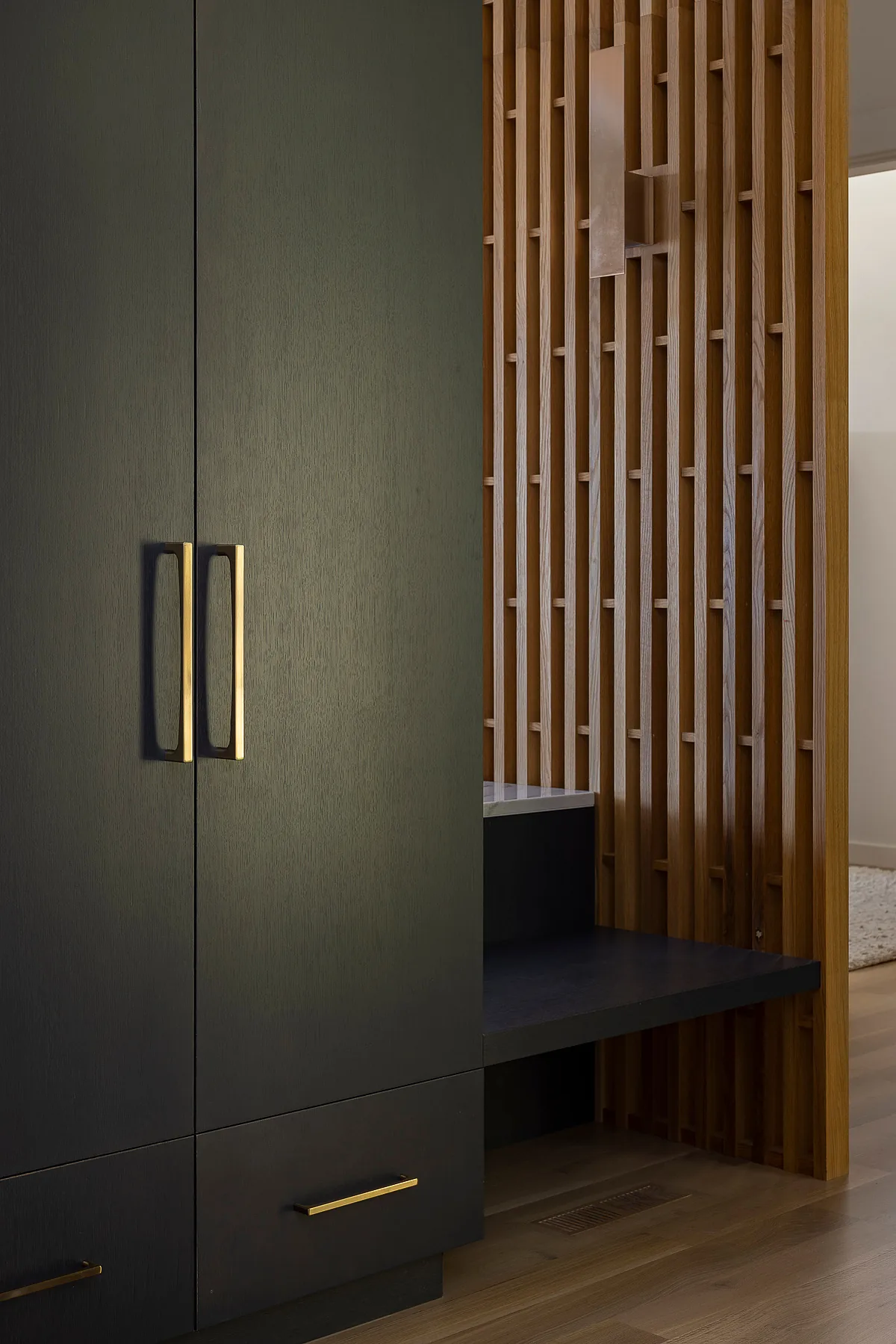 Dark wood cabinet with brass handles beside a wood slat divider in a modern interior space.