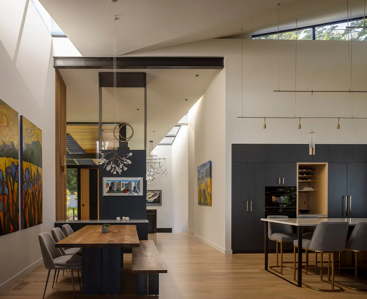 Dining space features a wooden table with bench and chairs, dark cabinetry, and modern pendant lighting under skylights.