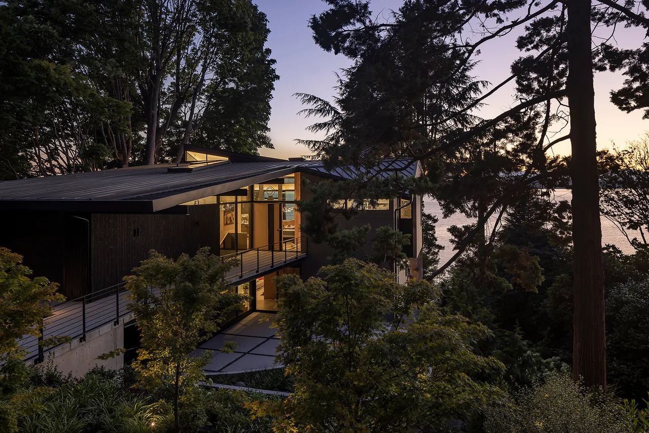 PERKINS LANE project with BAAN design features a modern home with a standing seam metal roof in a wooded setting by water in Seattle.