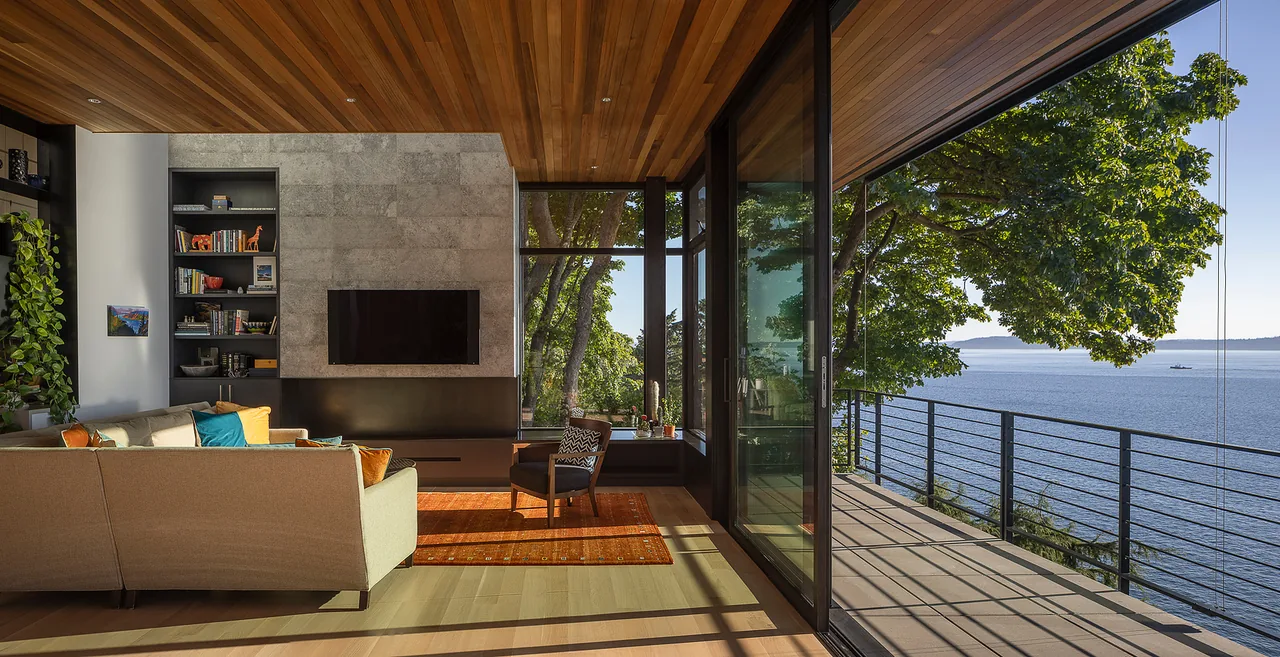 Living room with wood ceiling, concrete accent wall, floor-to-ceiling windows, and a balcony with water views at PERKINS LANE project.