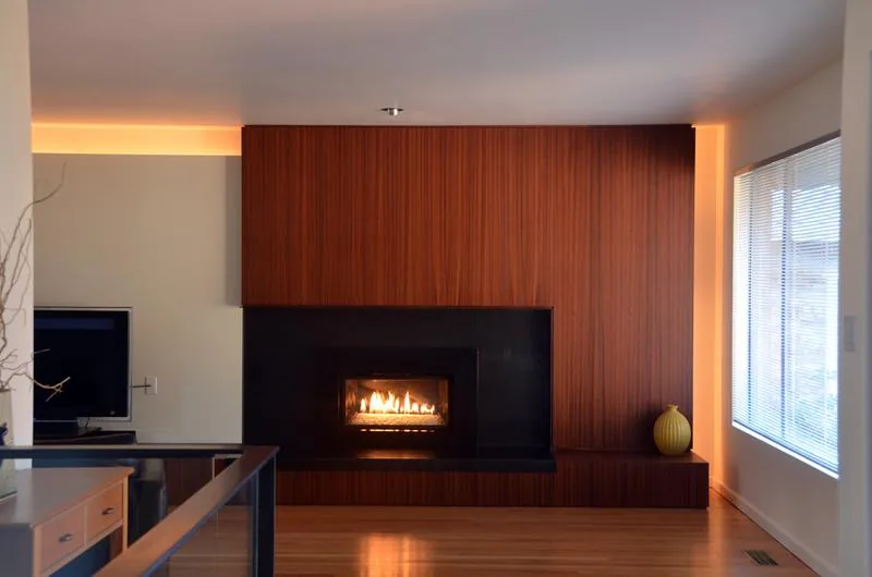 Living room with a fireplace recessed in a dark stone surround and wood-paneled wall with subtle LED lighting.