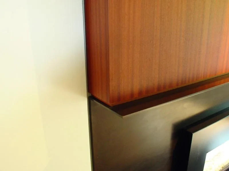 Vertical wood paneling is placed above a black blackened steel fireplace frame detail.