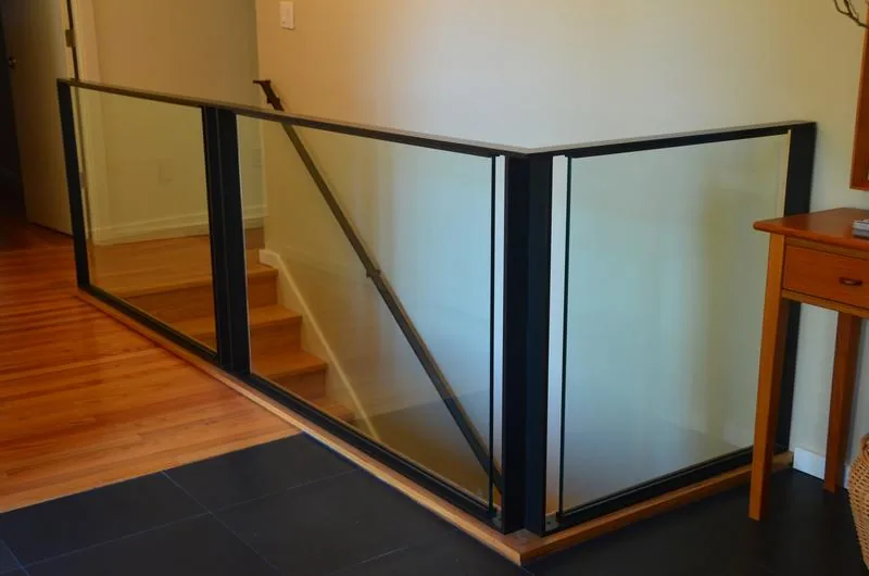 Modern stair railing features black frames and clear glass panels along a wood staircase.