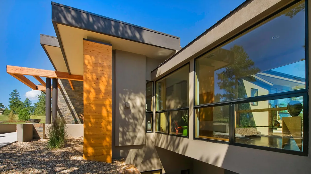 Modern residence facade with wood siding accents and expansive black-framed windows under a flat roof.