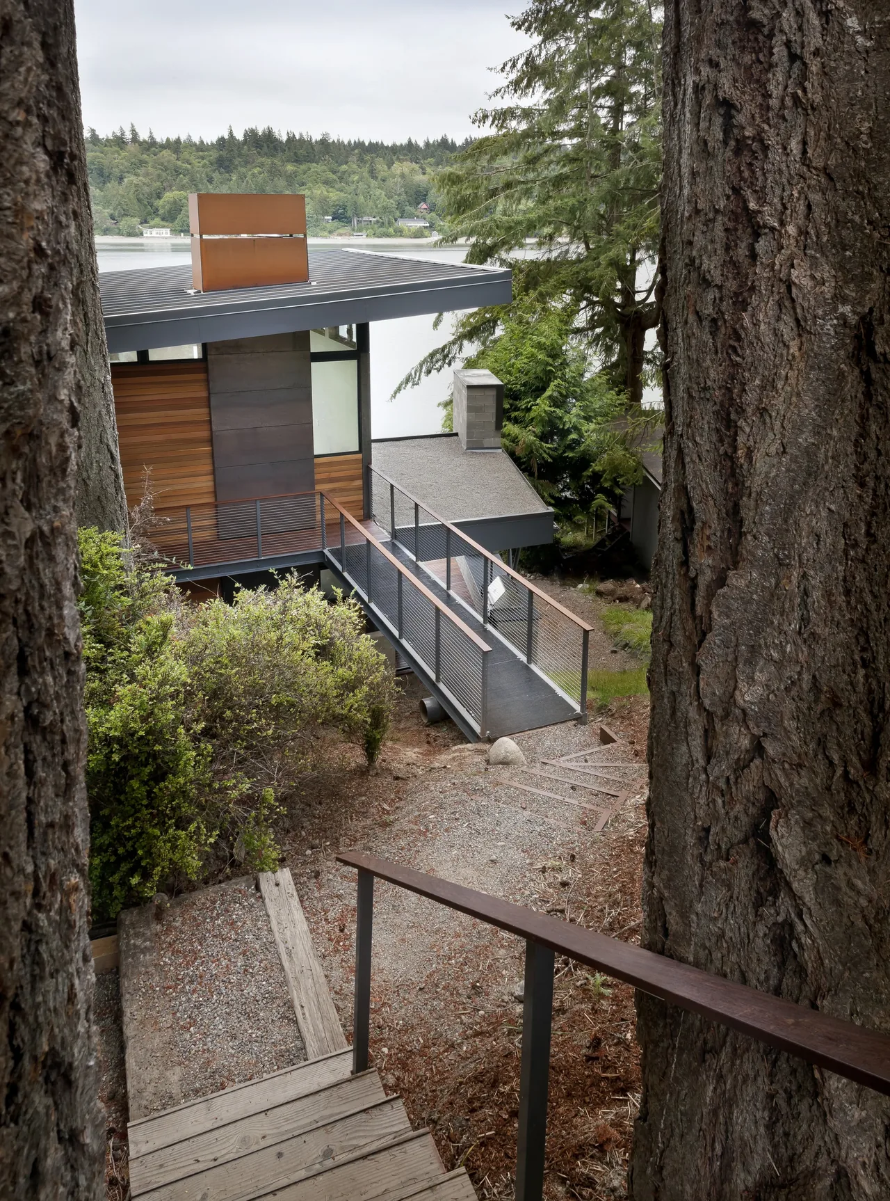 Herron Island Cabin features a modern design with metal roofing, wooden siding, and is situated in a wooded waterfront setting.