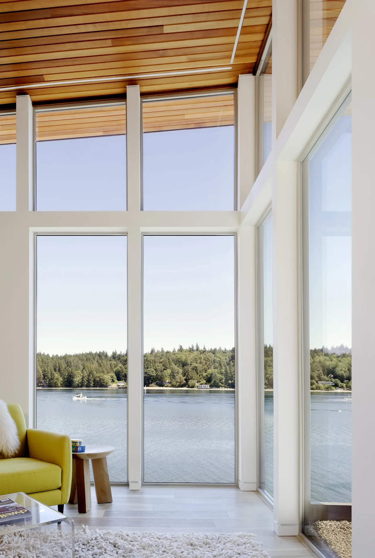 Living space with large floor-to-ceiling windows providing a clear lake view and forest backdrop.