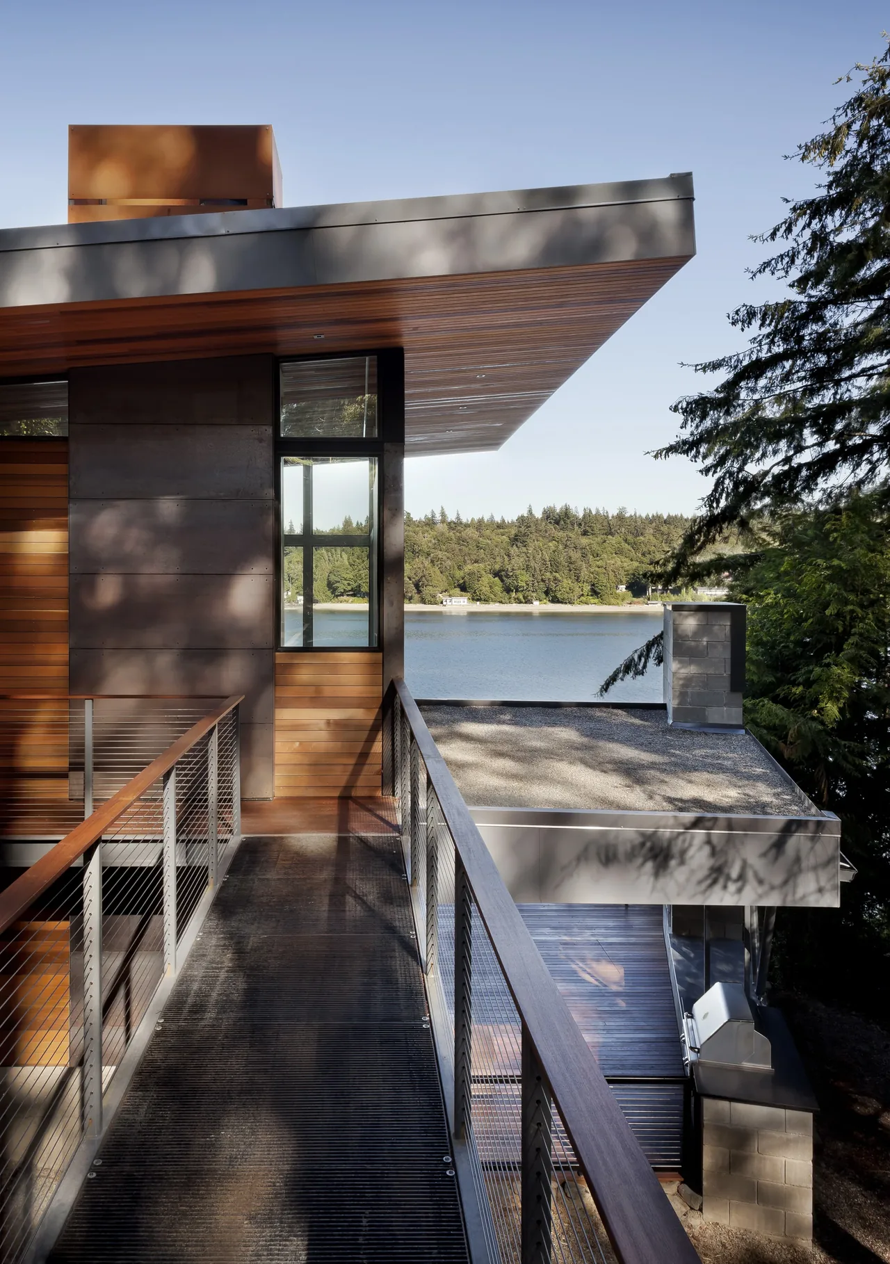 Herron Island Cabin features wood siding with metal accents and an overhanging flat roof, overlooking a peaceful lakeside setting.