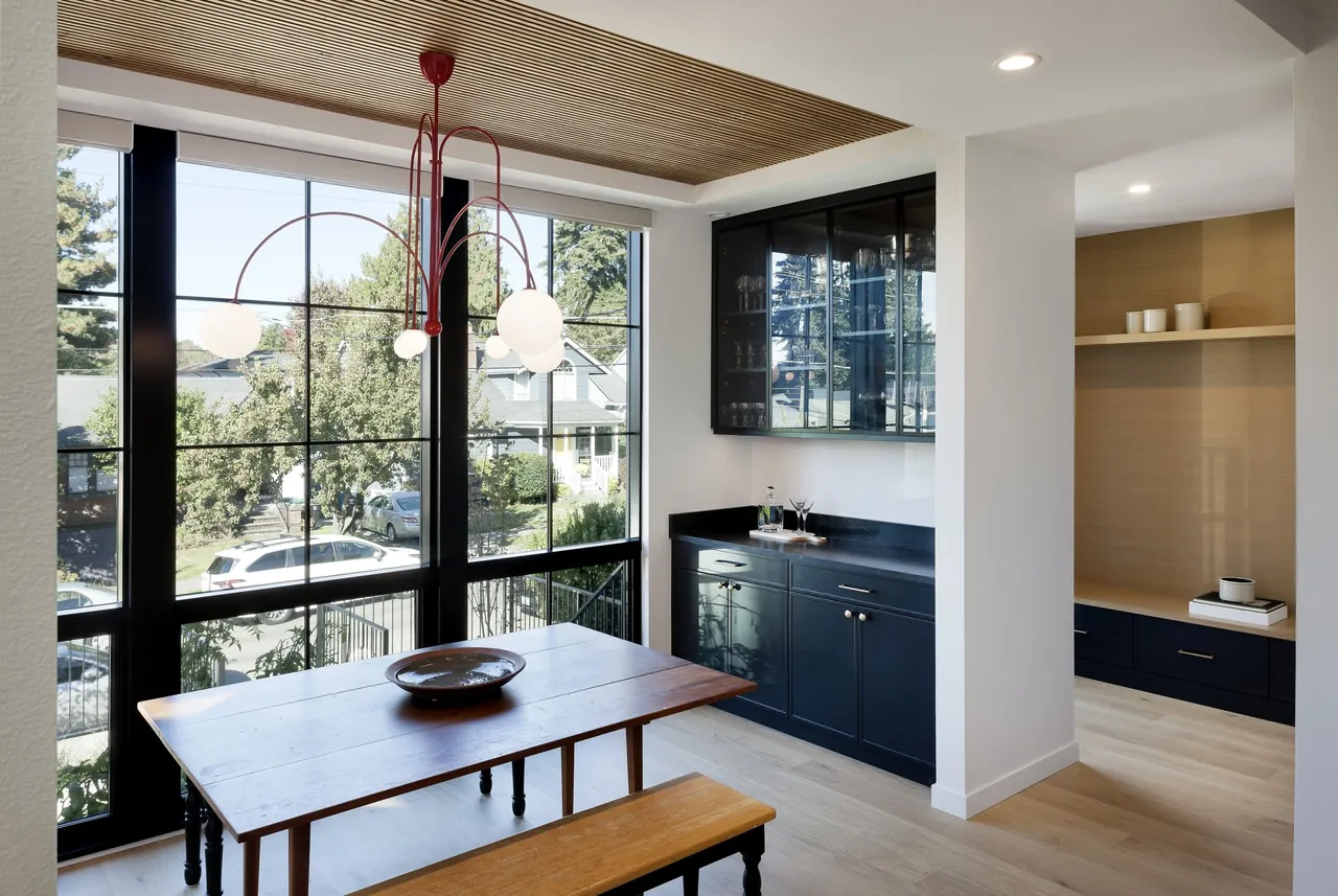 Dining room features black-framed grid windows and a wood slatted ceiling with a modern red chandelier over a wooden table.