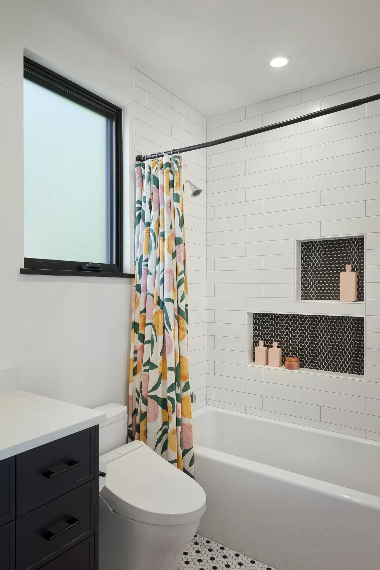 A bathroom featuring a white bathtub with built-in black hex tile shelves and a floral shower curtain.