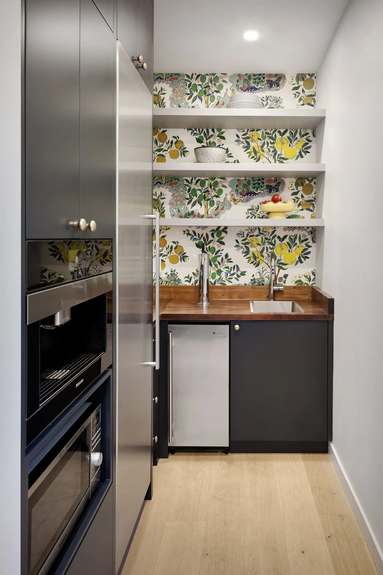 Kitchen nook featuring dark cabinets, stainless steel appliances, wood countertops, and floral wallpaper on the back wall.