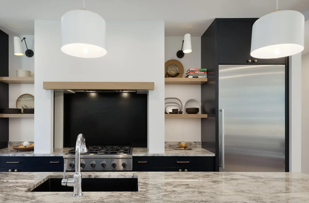 The Ravenna House kitchen features marble countertops, black cabinetry, stainless steel appliances, and wooden open shelving.