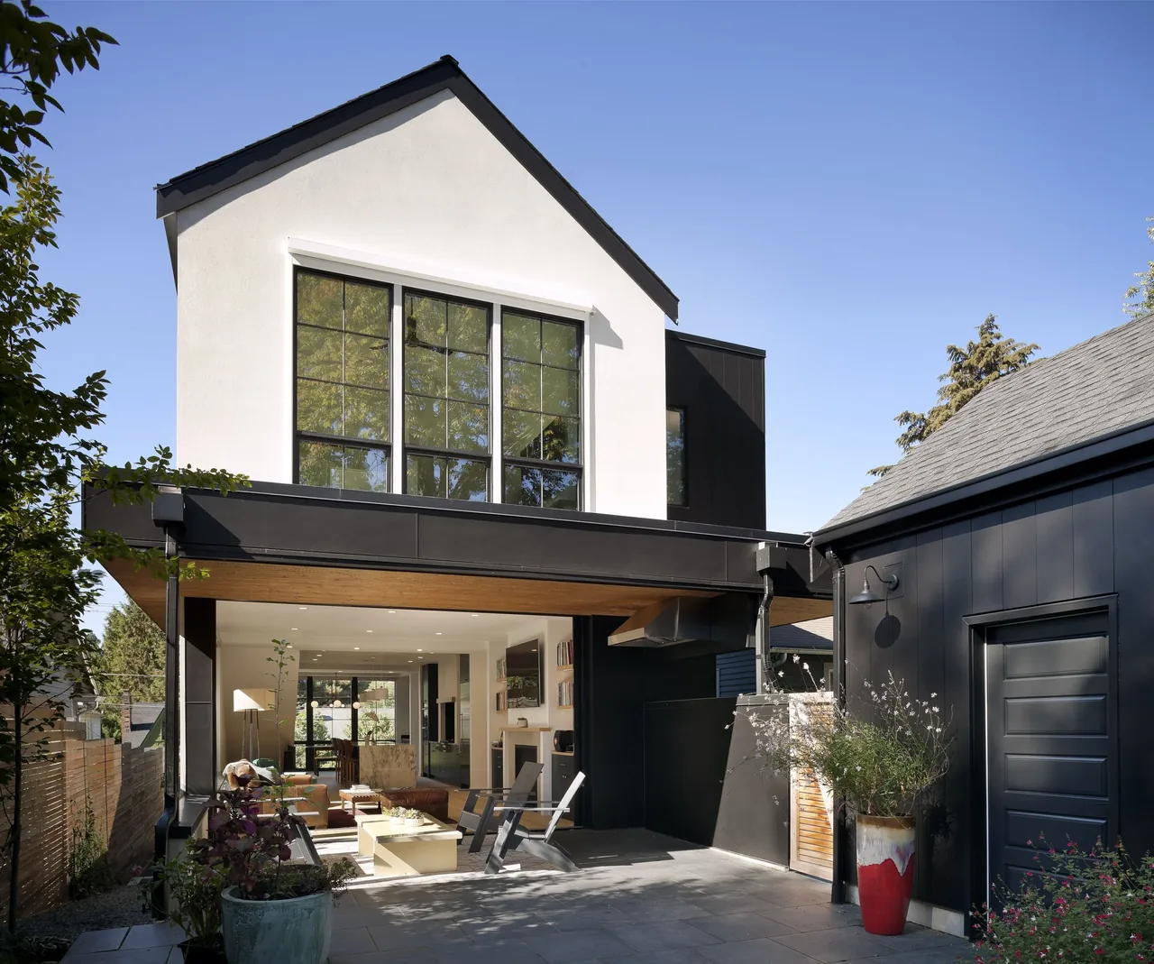 Outdoor view of a modern two-story house with large black-framed windows and an open patio seating area.