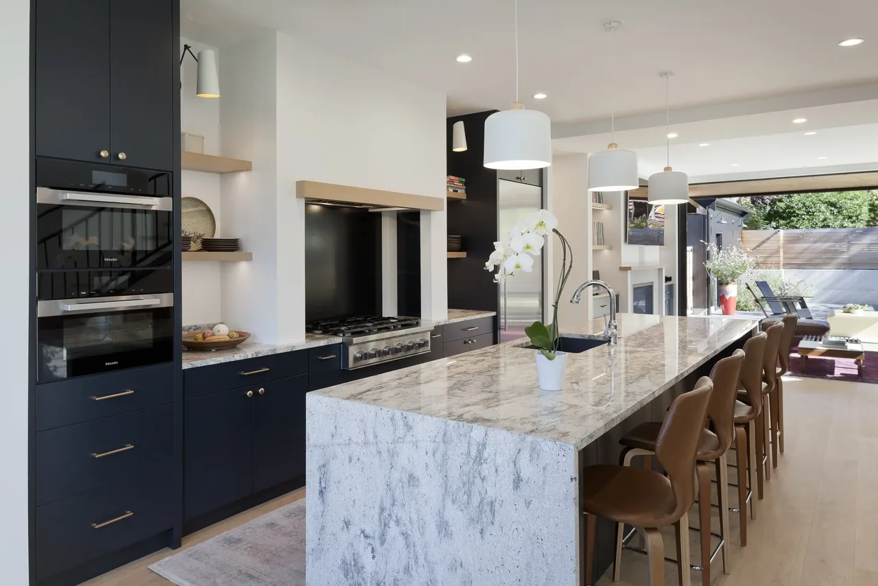 Modern kitchen with marble island, dark cabinets, pendant lights, and open views to an outdoor patio area.