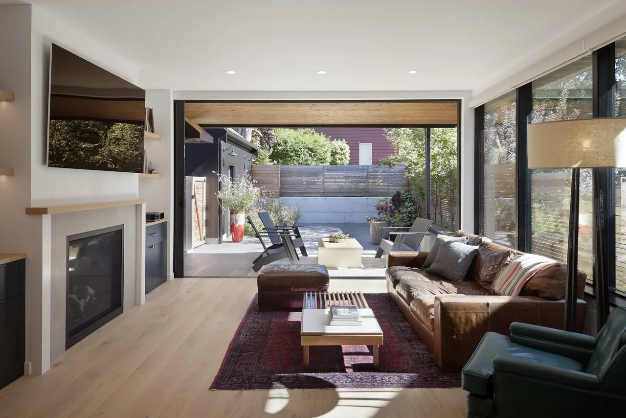 Living room featuring a leather sofa, fireplace, black window frames, and sliding glass doors opening to a wood-ceiling covered patio.