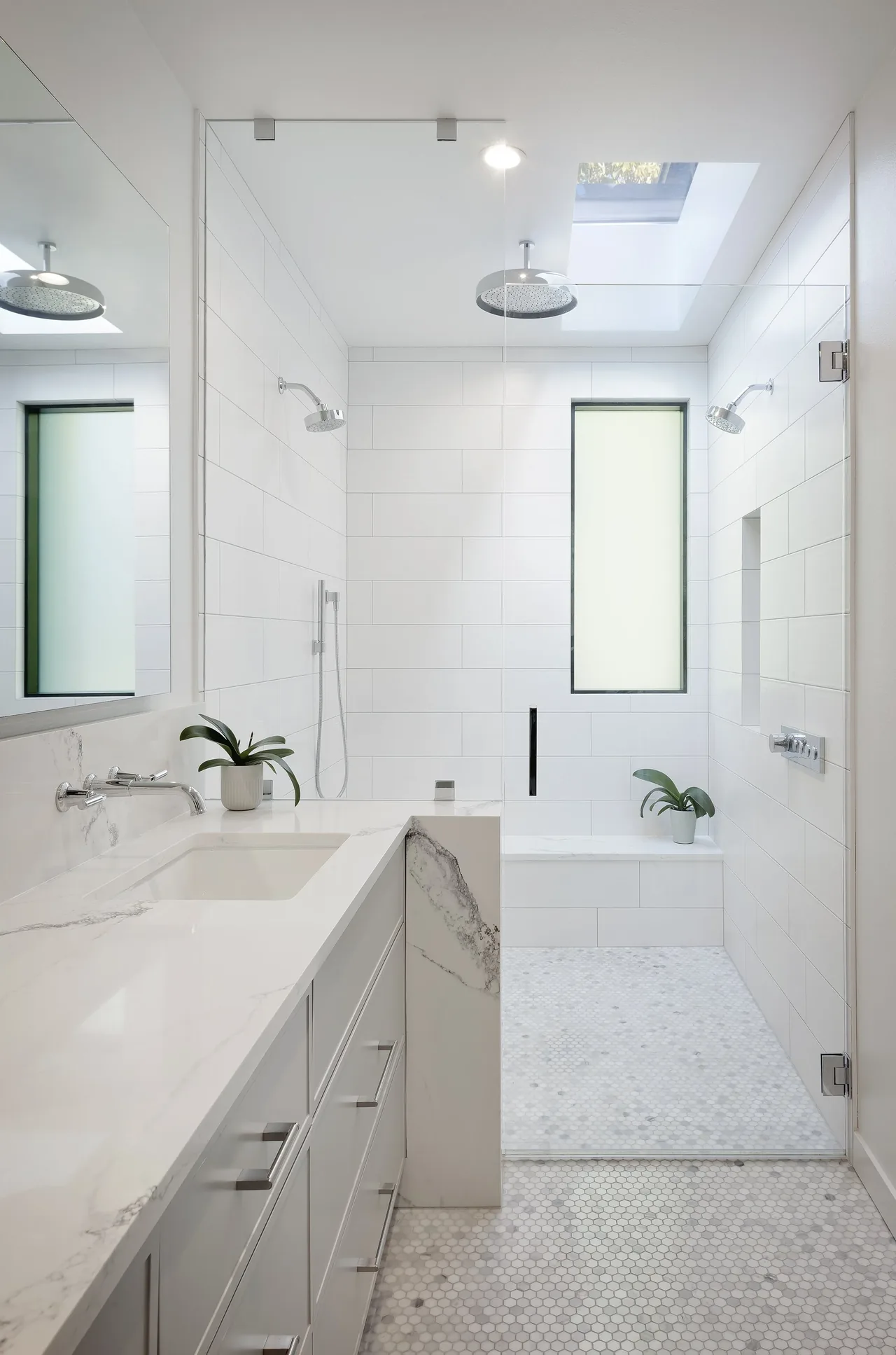 This Ravenna House bathroom features a double shower setup with a skylight and marble countertop vanity.