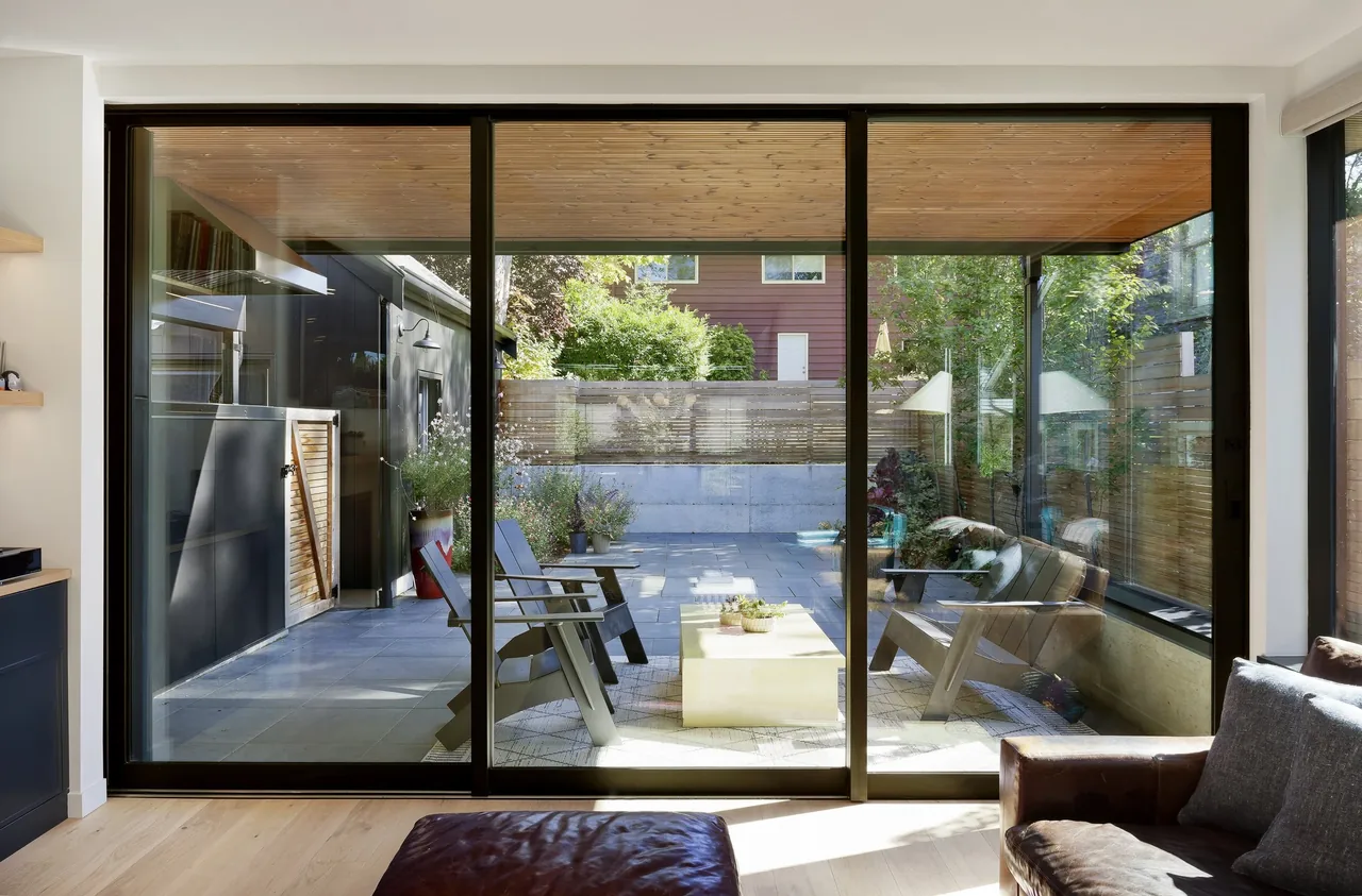 Covered outdoor patio with wood slatted ceiling visible from interior living space through black framed sliding glass doors.