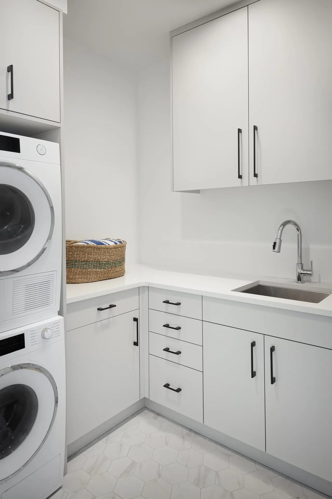 Laundry room featuring stacked washer and dryer, white cabinetry with black handles, and hexagonal tile flooring.