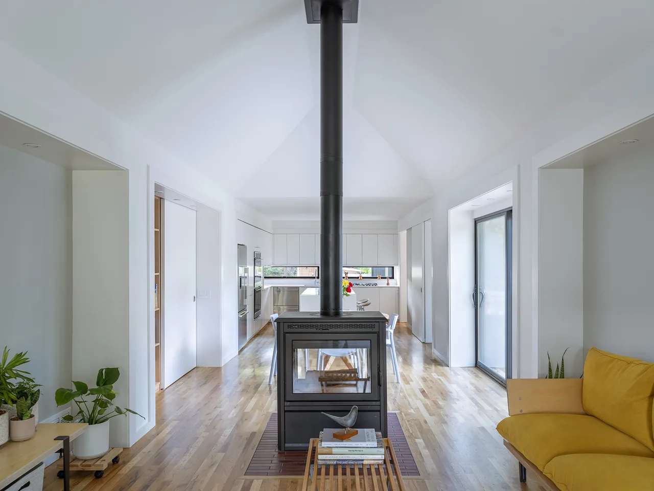 Open living and kitchen space with central wood stove and vaulted ceiling in a modern style home.