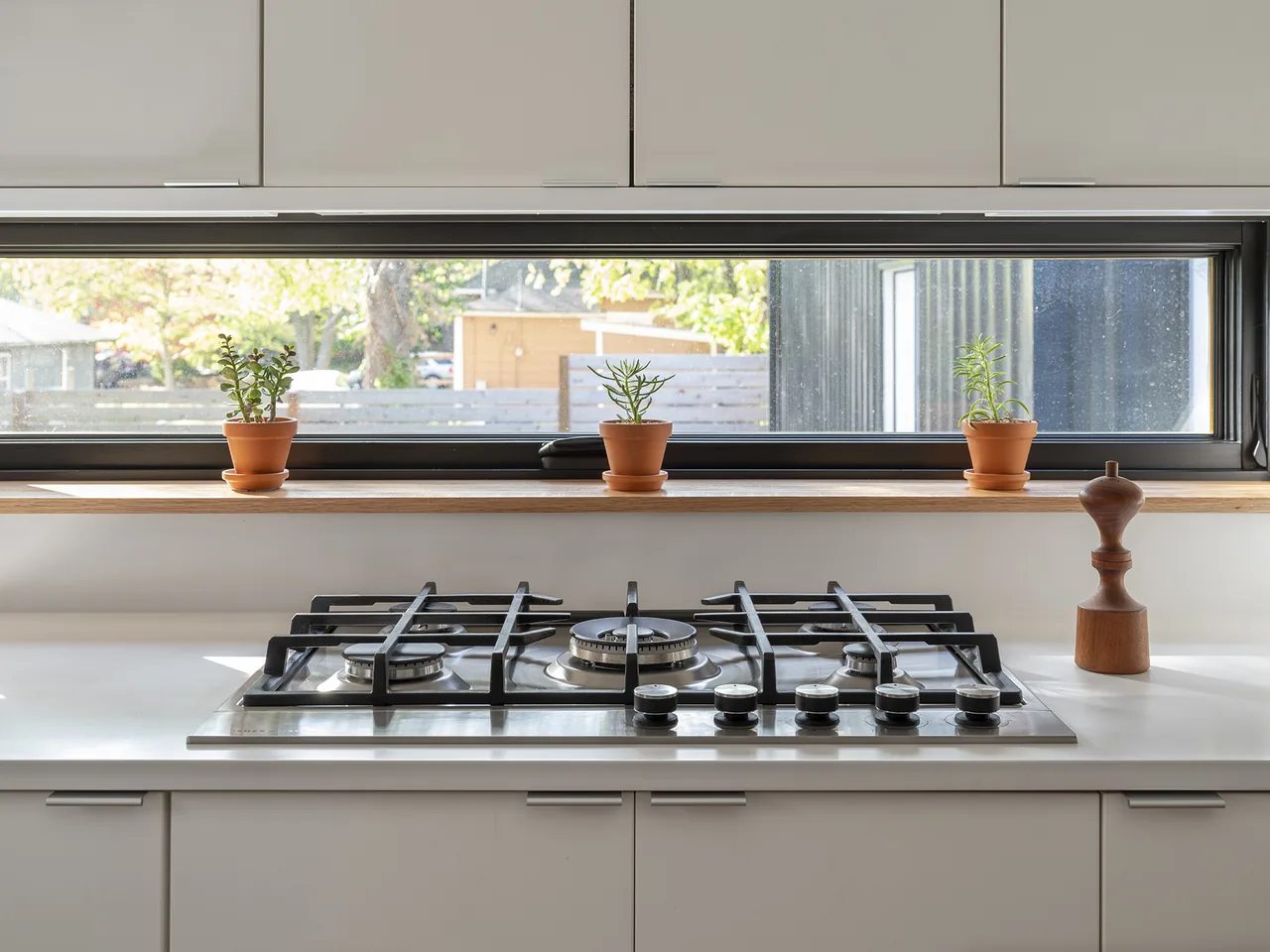 Modern kitchen gas cooktop beneath a long horizontal window with terracotta pots on the sill.
