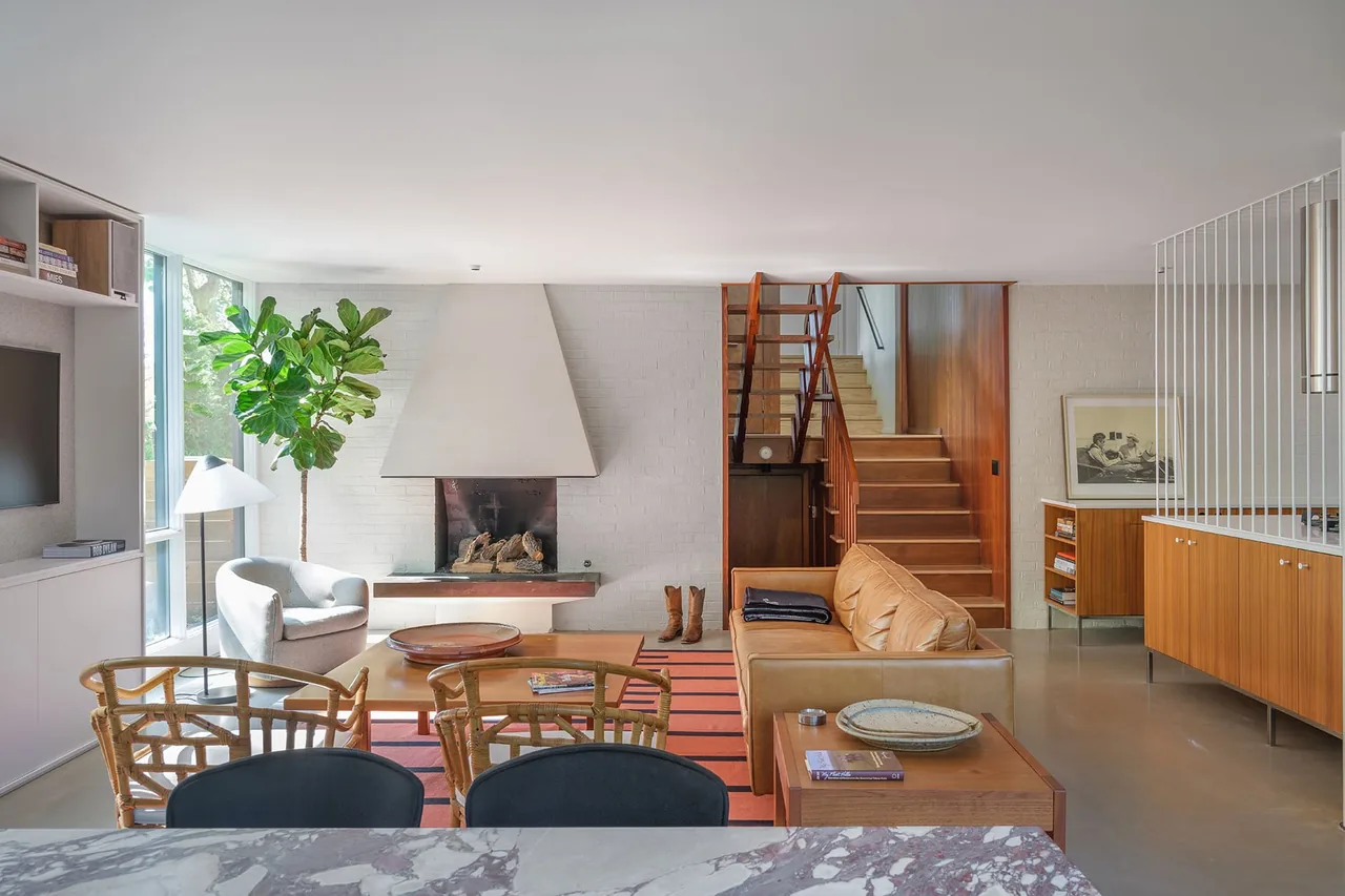 Living room in the Kivett Redux project features a fireplace, wood cabinetry, and a modern stair design.