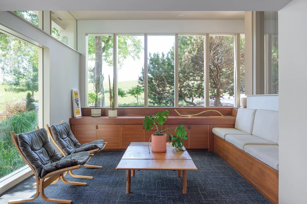 Living area in the Kivett Redux project with floor-to-ceiling windows and wooden built-in bench seating by Forward Design Architecture.