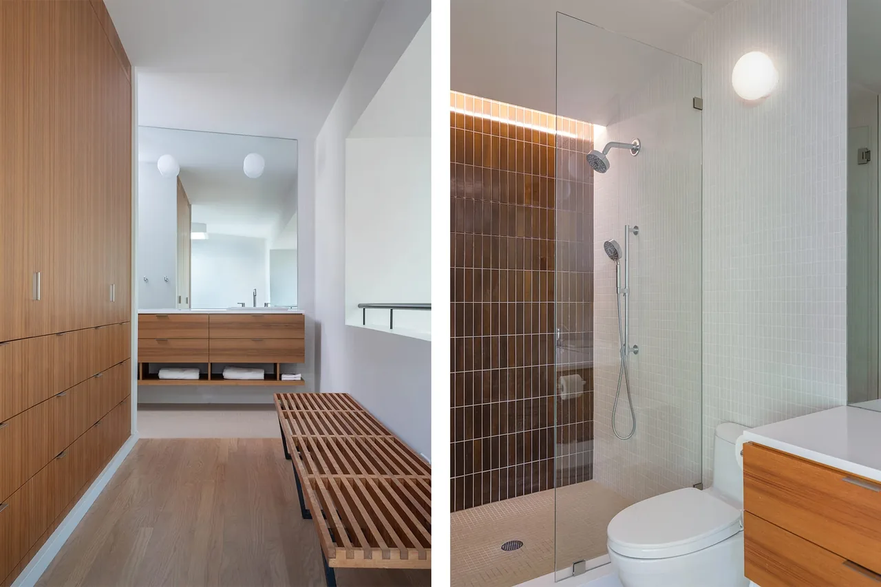 Modern bathroom features wood cabinetry, a slatted wood bench, and a glass shower with brown vertical tile accent.