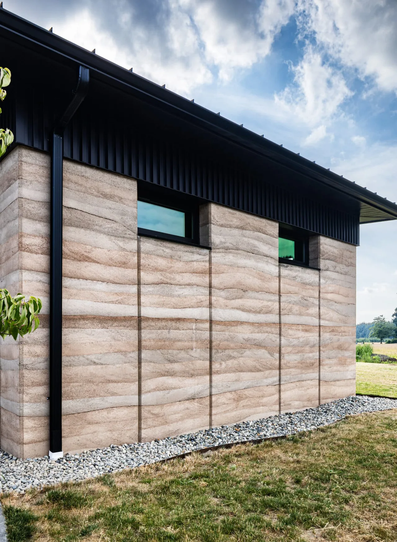 Rammed earth wall with narrow horizontal windows and black metal siding below a shed roof.