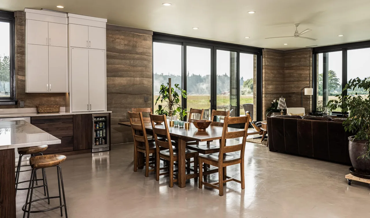 Open dining and kitchen area with floor-to-ceiling glass doors and rammed earth walls provides natural light and outdoor views.