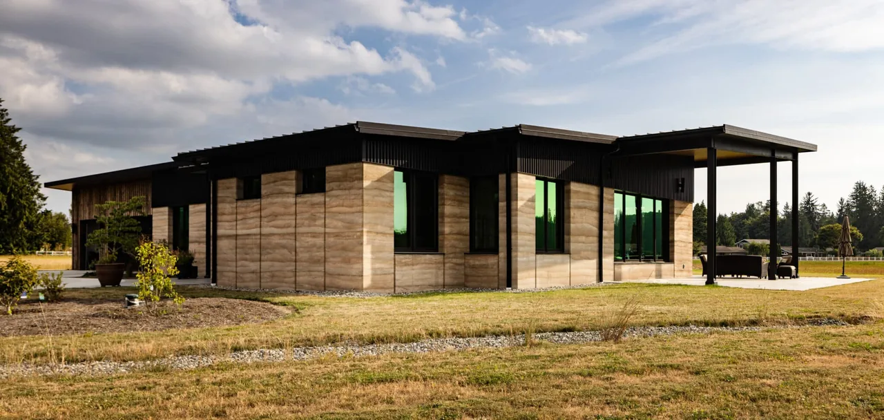 Rammed Earth House features black framed windows and a flat sloped roof with an outdoor covered patio area.