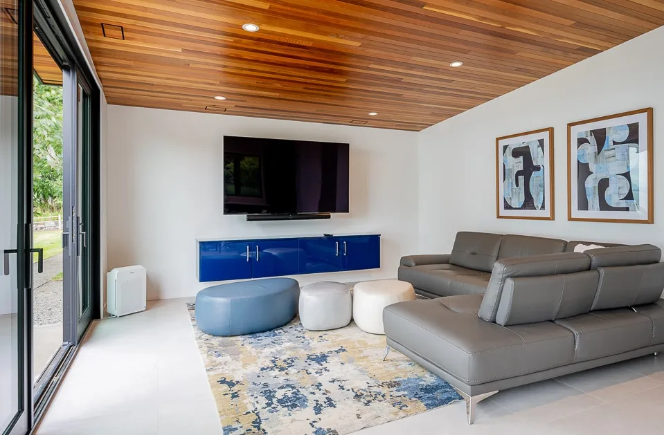 Living room with leather sectional, wall-mounted TV, blue media cabinet, and wood ceiling in the Cliff House ADU project.