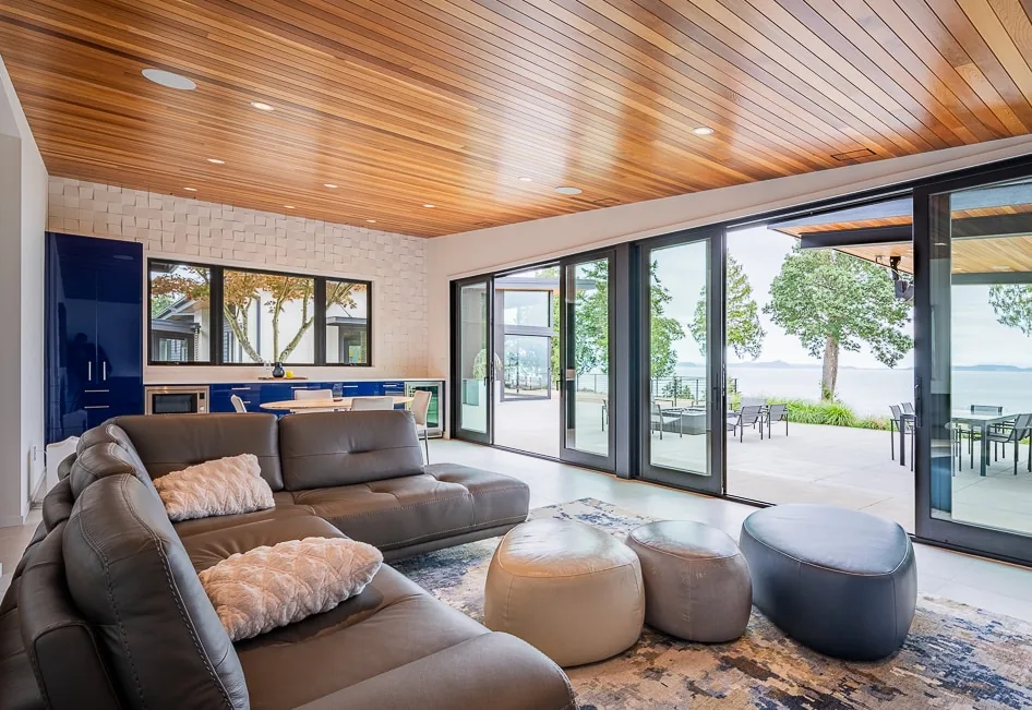 Living space with leather sofa and ottomans opens to a large patio with ocean views through sliding glass doors.