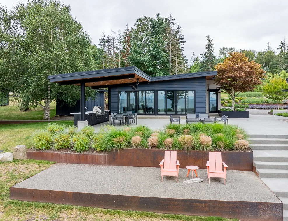 Cliff House ADU features an outdoor living area with a metal planter box and seating across from a contemporary structure with floor-to-ceiling glazing.