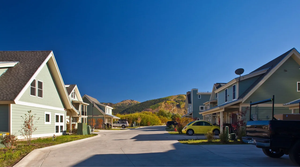 Snow Creek Cottages feature light blue exteriors in a three-story design with a paved street and surrounding hills visible.