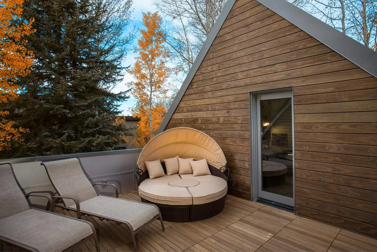 Outdoor deck area featuring wood siding with folding glass door and cushioned seating including a round daybed with a canopy.
