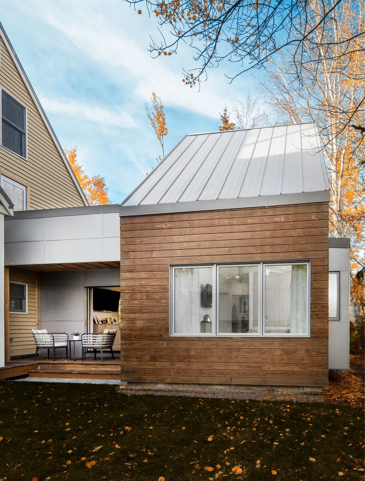 Modern small house extension with wood siding and a standing seam metal roof next to a deck with seating.