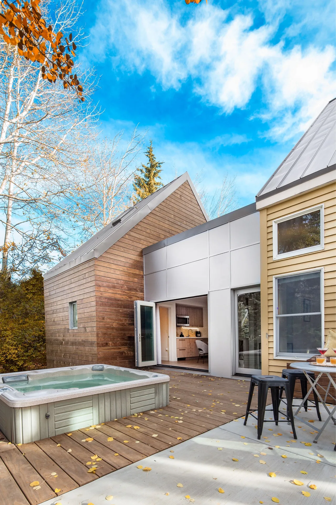 Patio with hot tub and open folding doors to kitchen in a mixed-material house combining wood siding and metal panels.