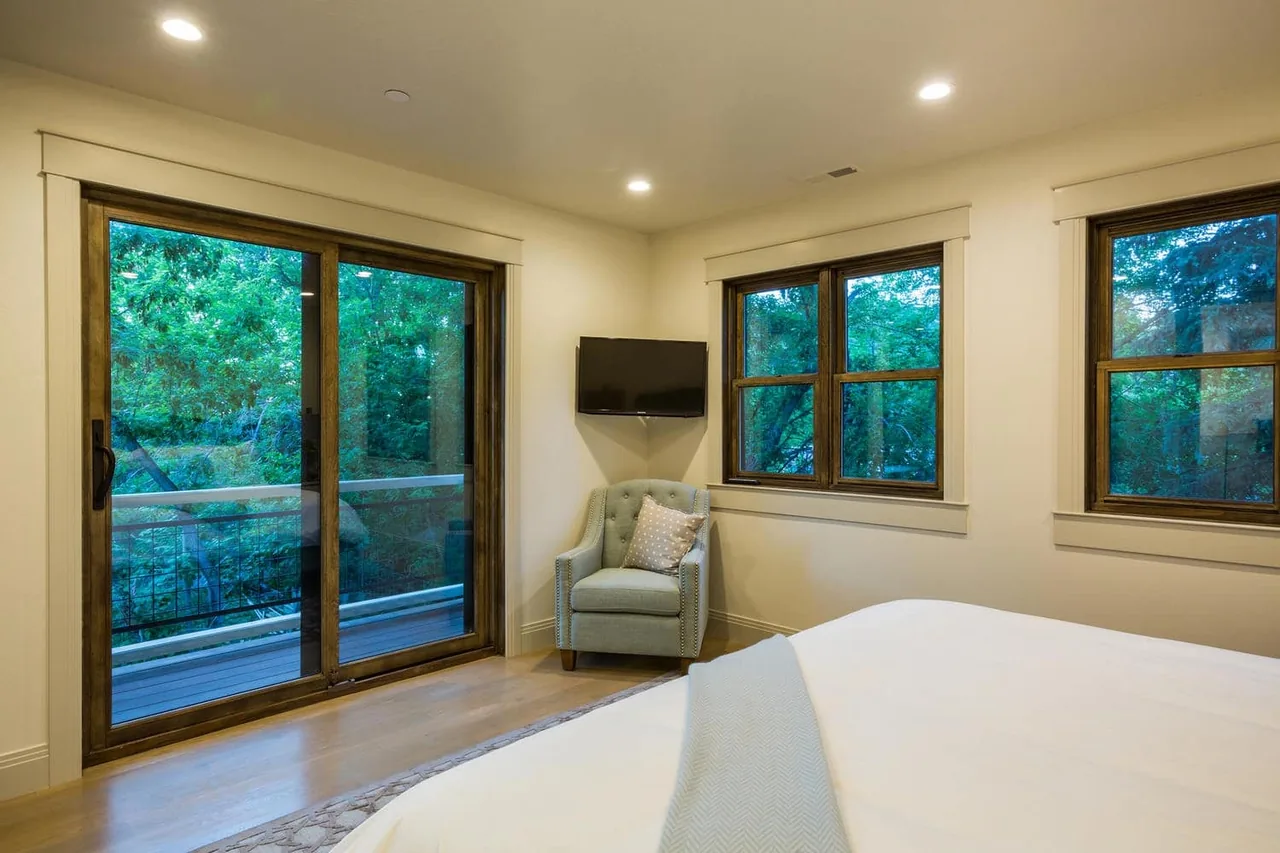 Bedroom with wood window frames and sliding glass door opening to a balcony with metal railing.
