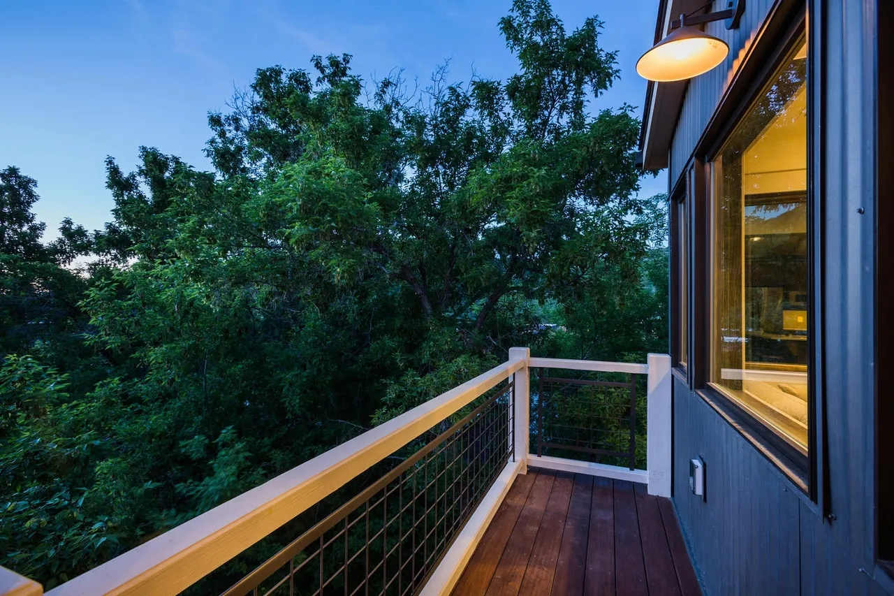 Outdoor balcony with wooden decking and white railing adjacent to a modern house with large window.