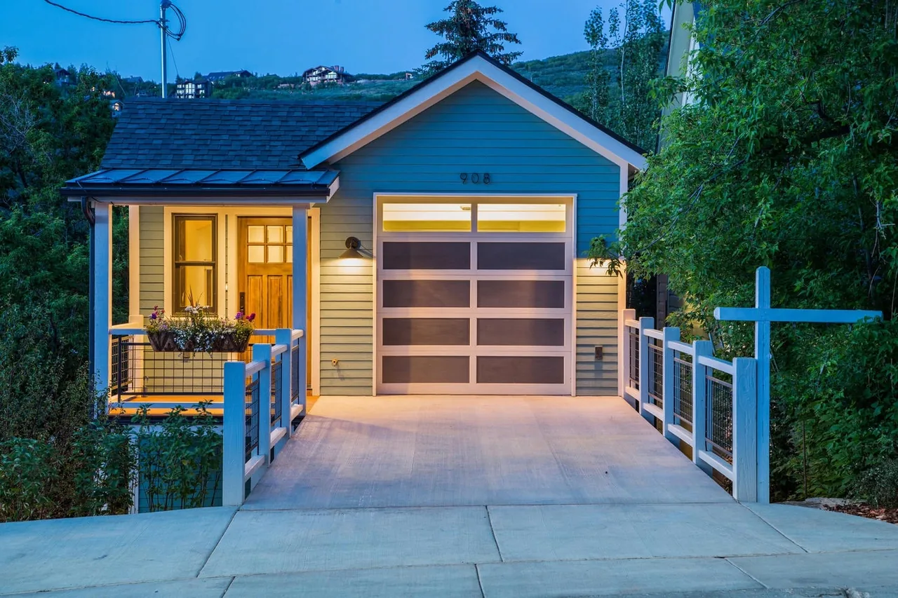 Exterior front view of Norfolk Ave 1 house featuring a blue facade, wood door, and illuminated wire-railing porch at dusk.