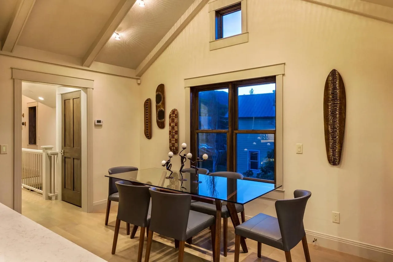 Dining room with glass table, gray chairs, and wooden window frames under vaulted ceiling at Norfolk Ave 1.