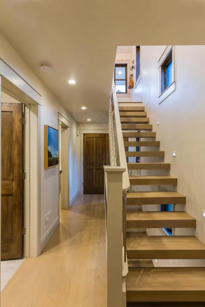Hallway view featuring floating wood stairs with white railing and recessed lighting.