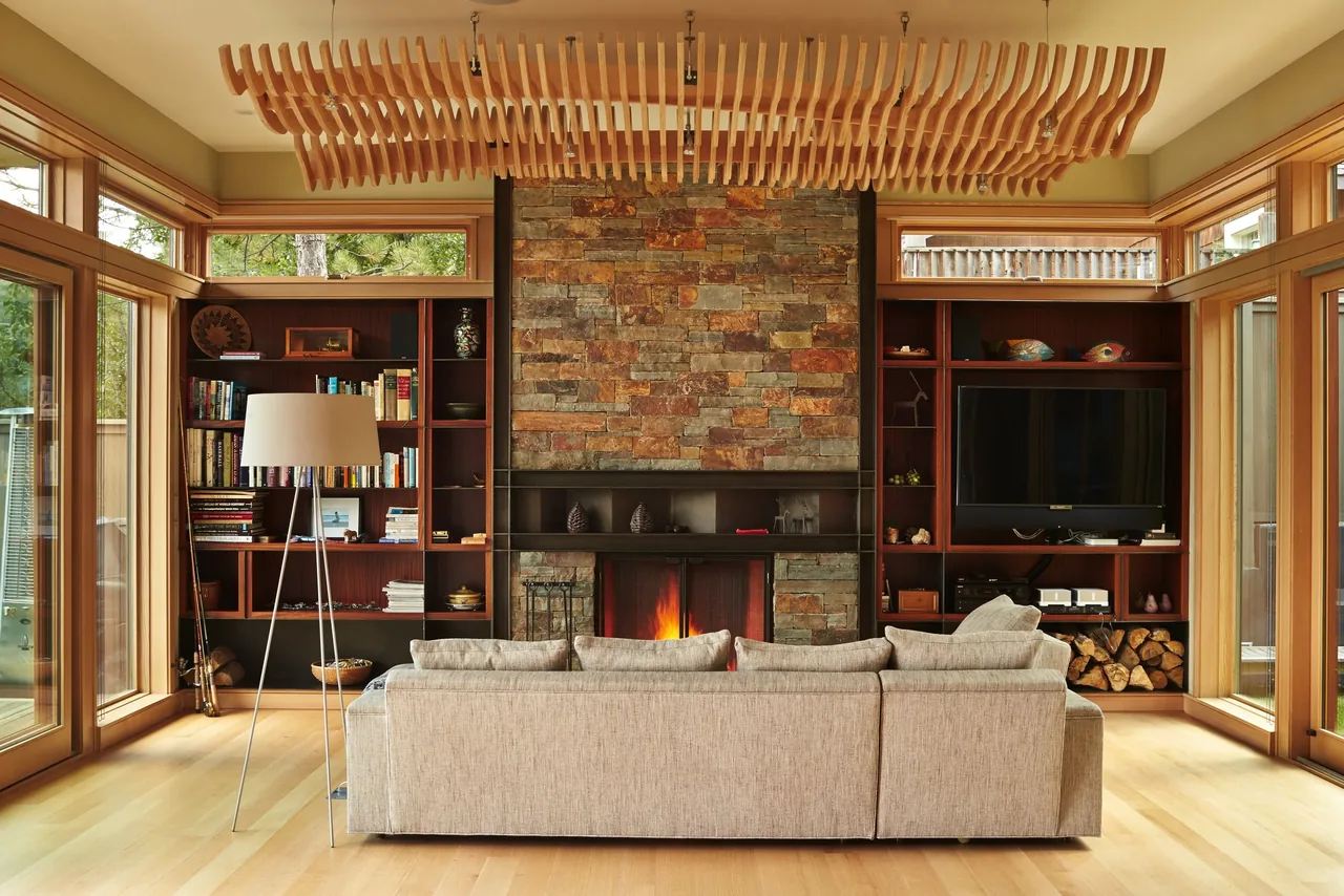 Living room features a central stone fireplace flanked by built-in wooden shelves and large wood-framed windows.