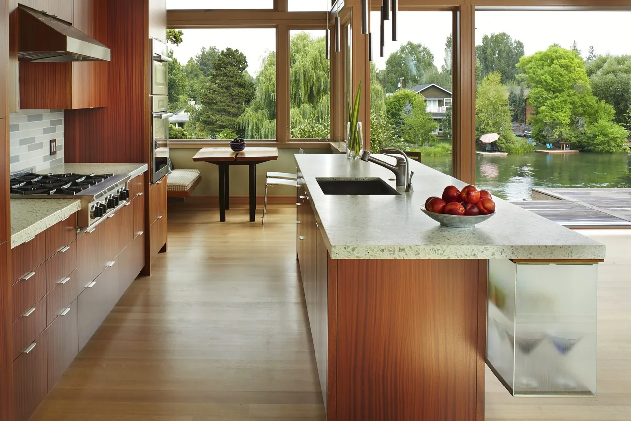 This kitchen features wood cabinets, a large island with a built-in sink, and large windows offering a lake view.