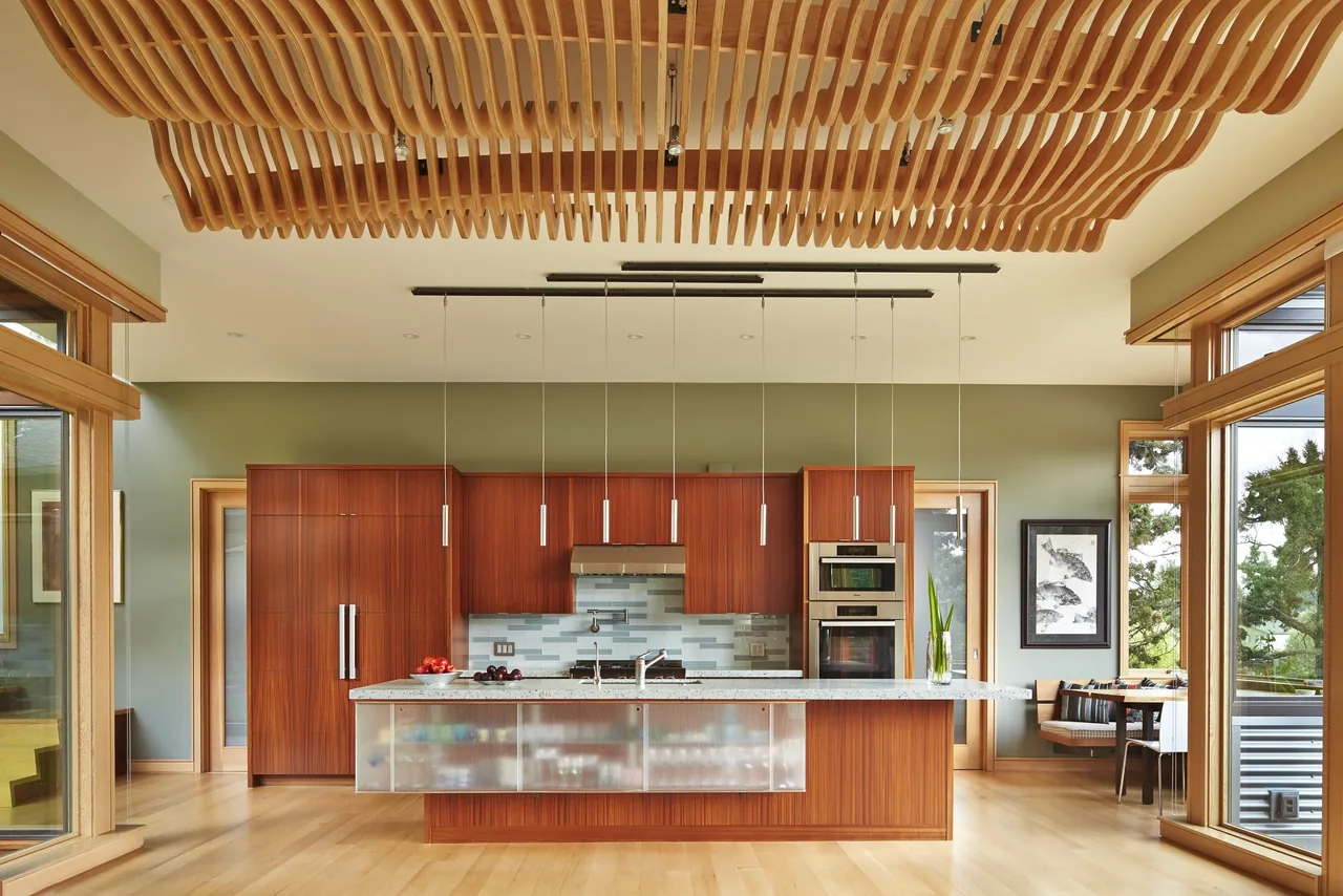 Kitchen in the Deschutes project by FINNE Architects features wood cabinetry and a wooden slat ceiling installation.