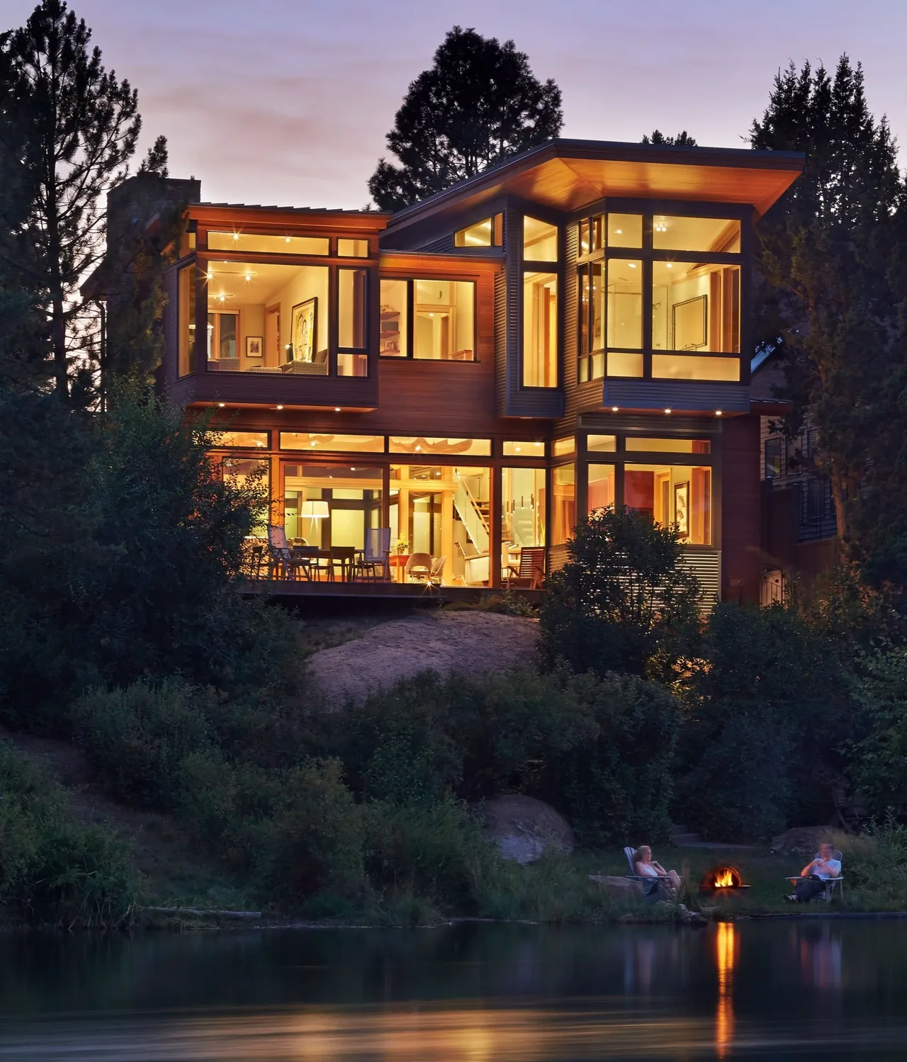 The Deschutes house features floor-to-ceiling glass walls overlooking natural landscaping and a lakeside fire pit.