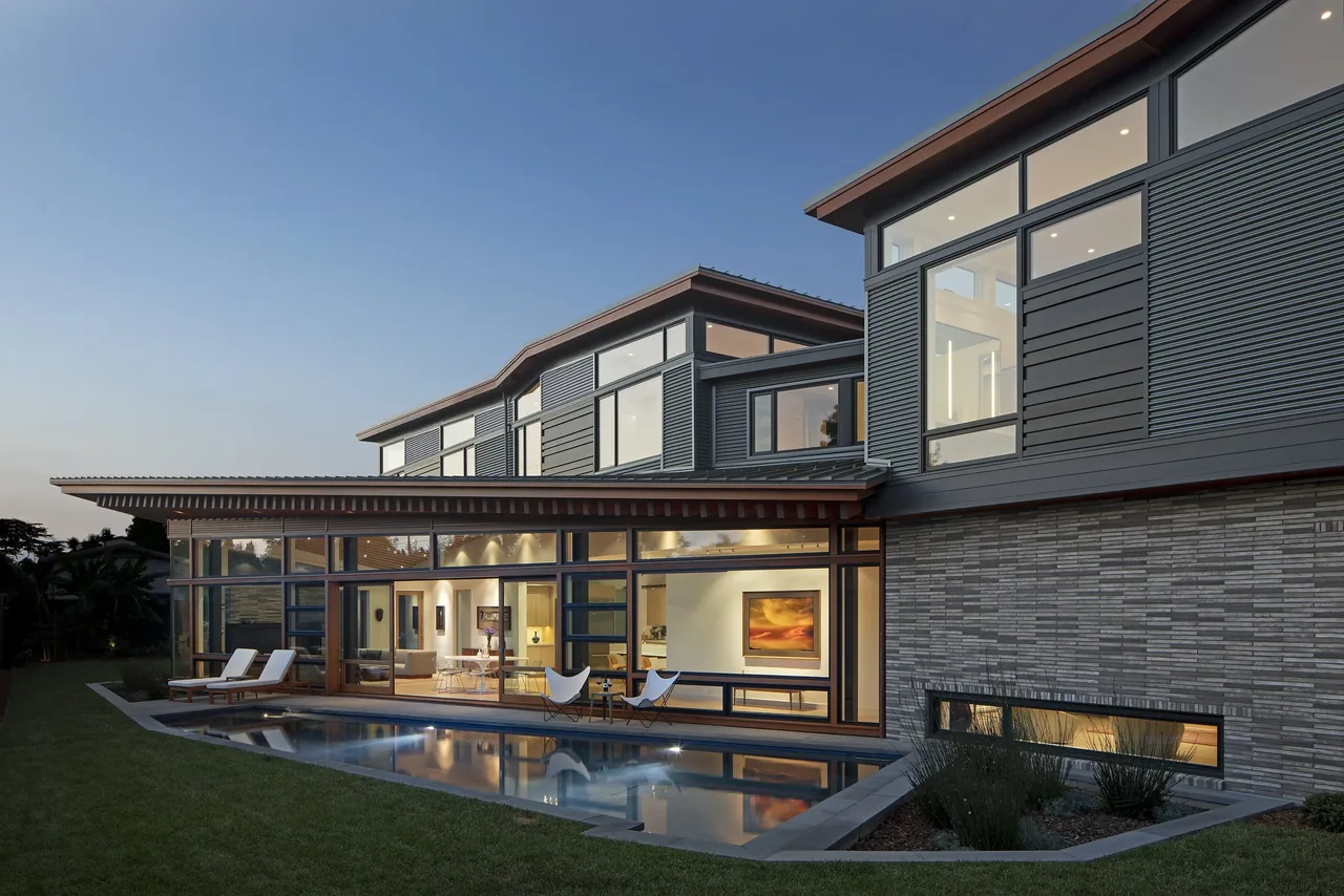 Modern two-story home with extensive glazing and a slim lap pool at dusk.