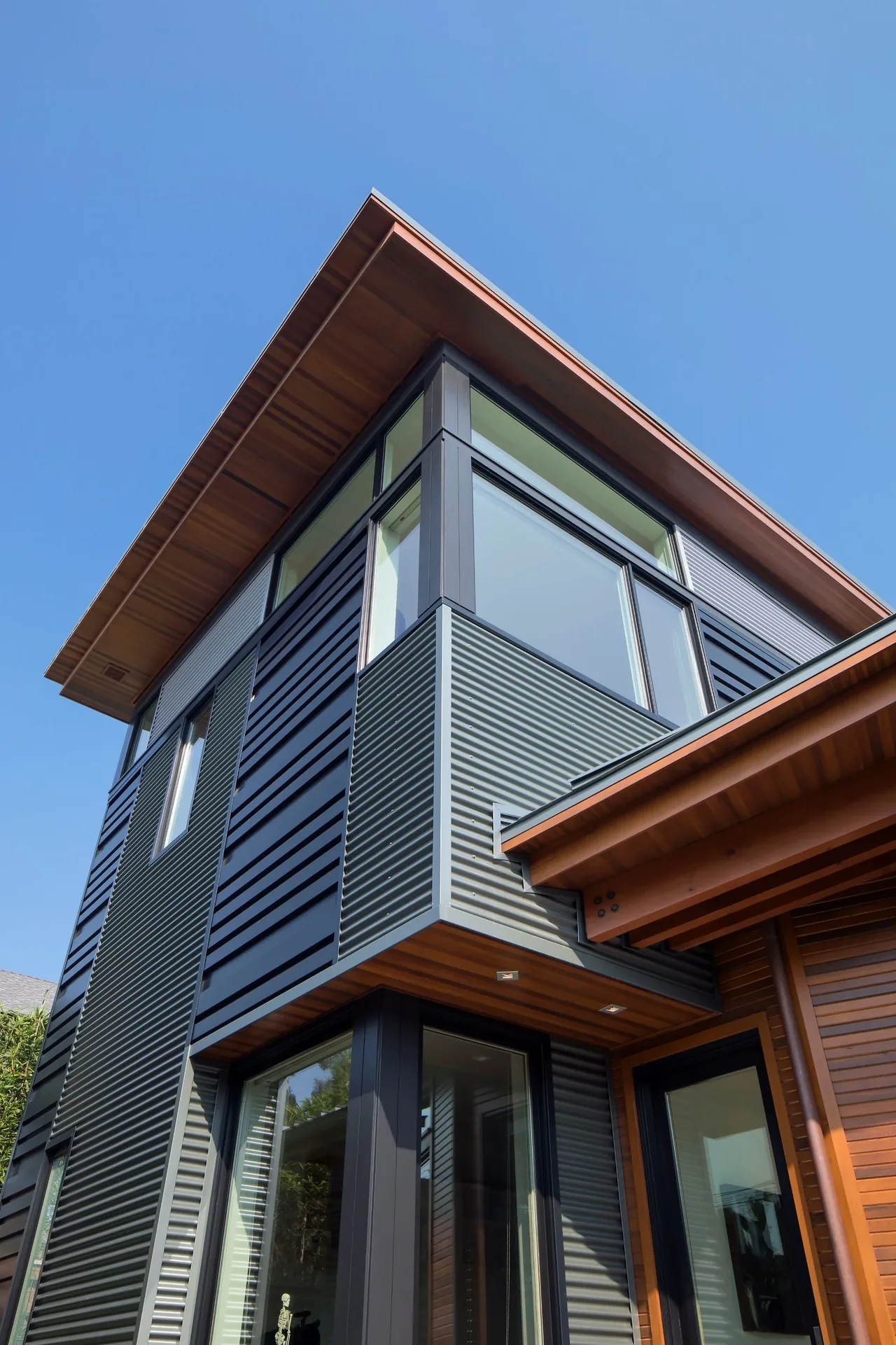 Exterior corner of a modern home featuring corrugated metal siding with wood soffits and large windows by FINNE Architects.