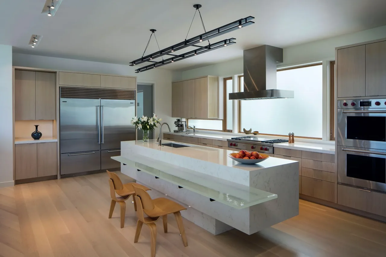 The Venice kitchen features light wood cabinetry, a long island with hung glass countertop, and stainless steel appliances.
