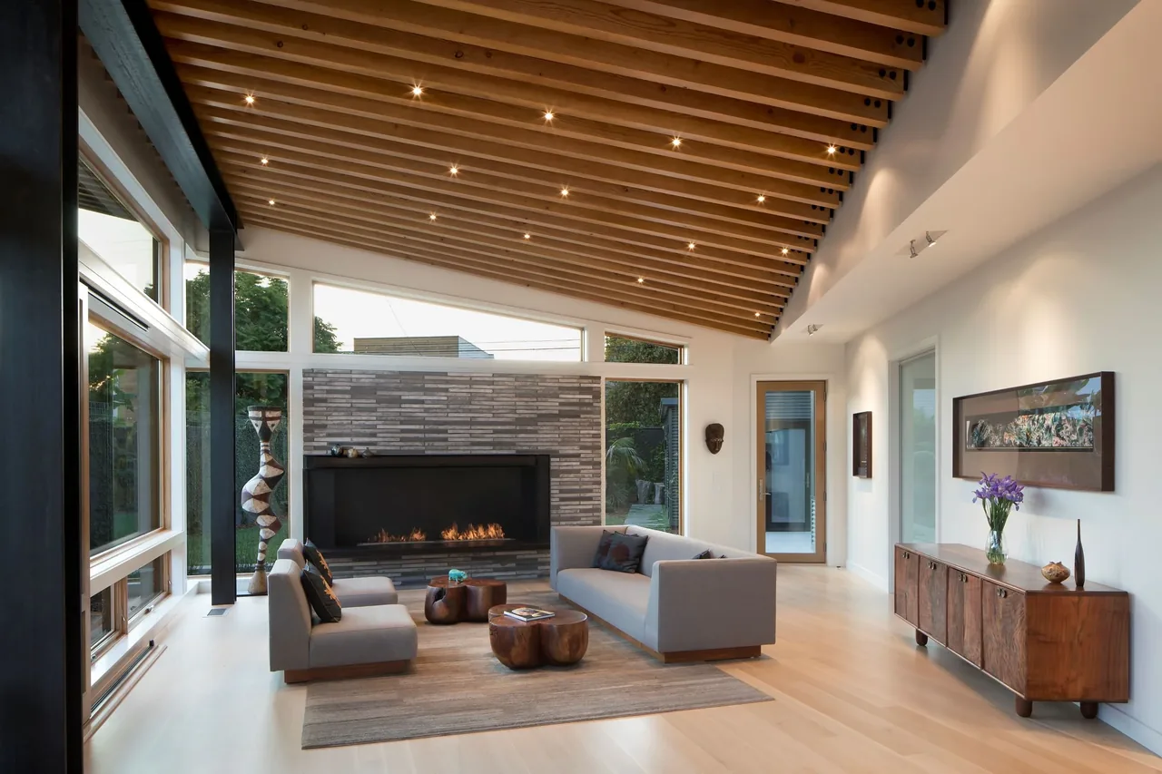 Living room features light hardwood flooring, a sloped ceiling with exposed wood beams, and a linear fireplace with tile surround.