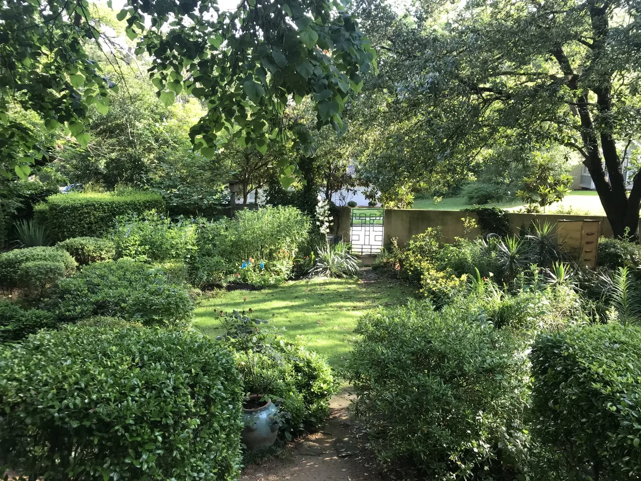 The Harmon Residence garden features dense greenery with trimmed bushes and a decorative metal gate.